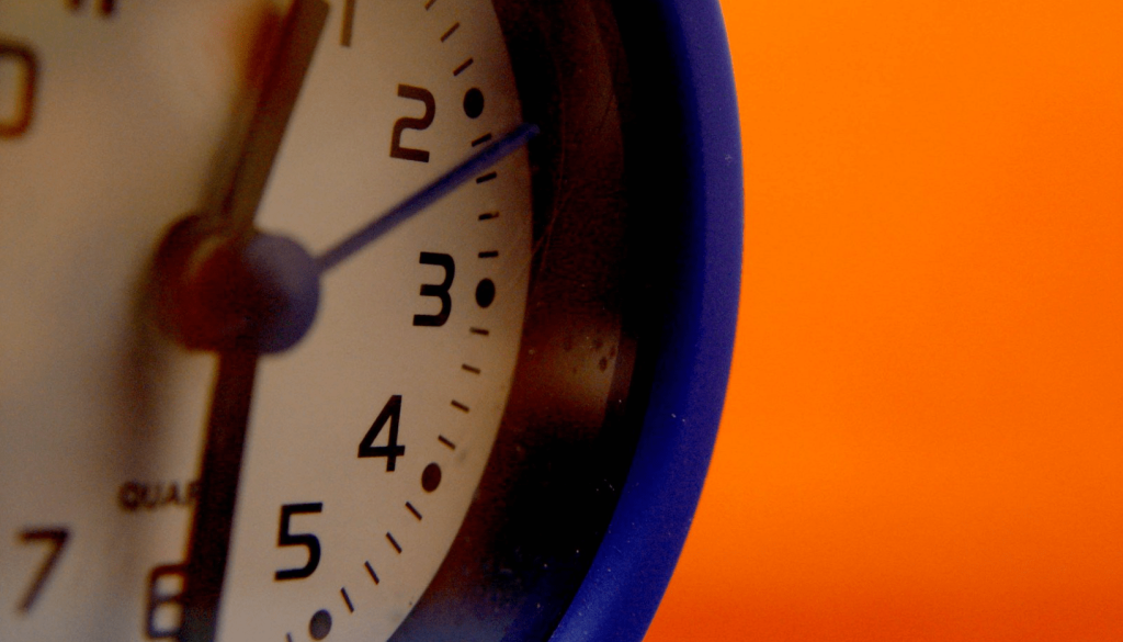 Image of a blue clock with an orange background for an article about meeting the demand in sourcing and procurement.