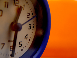 Image of a blue clock with an orange background for an article about meeting the demand in sourcing and procurement.